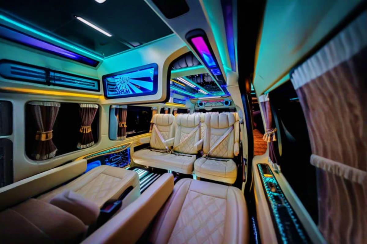 Luxury van interior with cream leather seats, neon cyan and magenta lighting, and large windows during nighttime airport tran