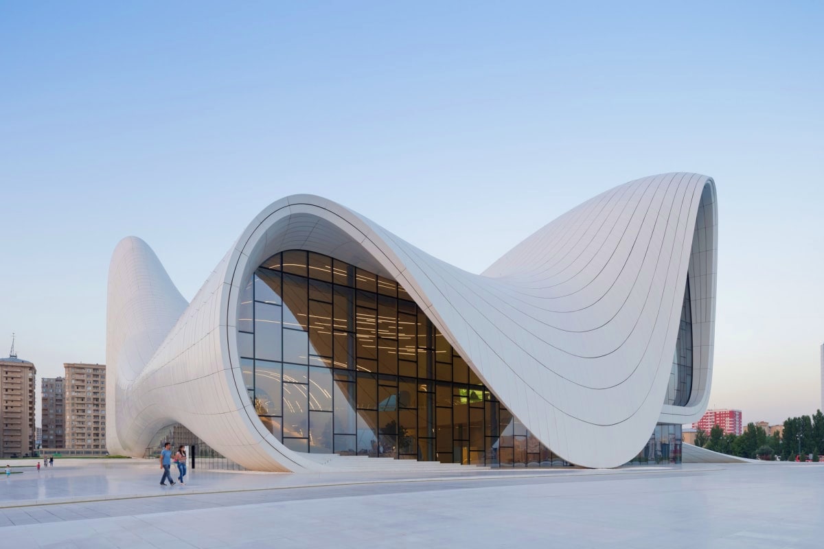 Modern white curved building with flowing architectural design, large glass windows, and plaza with visitors in Baku city