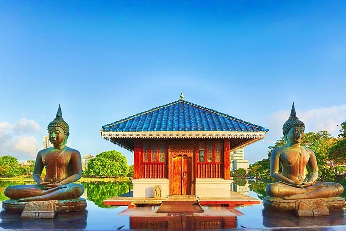 Colombo City Tour by Tuk Tuk Buddhist temple with blue tiled roof and red doors flanked by two large bronze Buddha statues in meditation pose on water