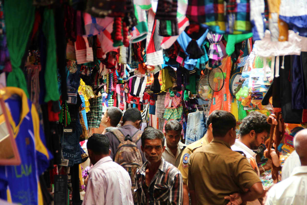 Crowded street market in Colombo with colorful hanging clothing and textiles, local shoppers browsing stalls