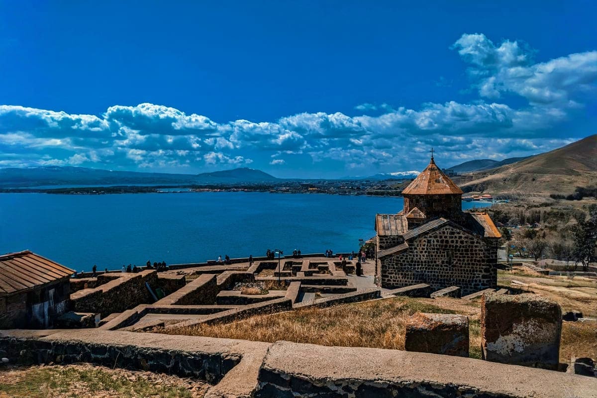 Day trip to Tsaghkadzor and Lake Sevan tour from Yerevan Sevan Monastery stone church with conical dome overlooking bright blue Lake Sevan waters under clear sky in Armenia