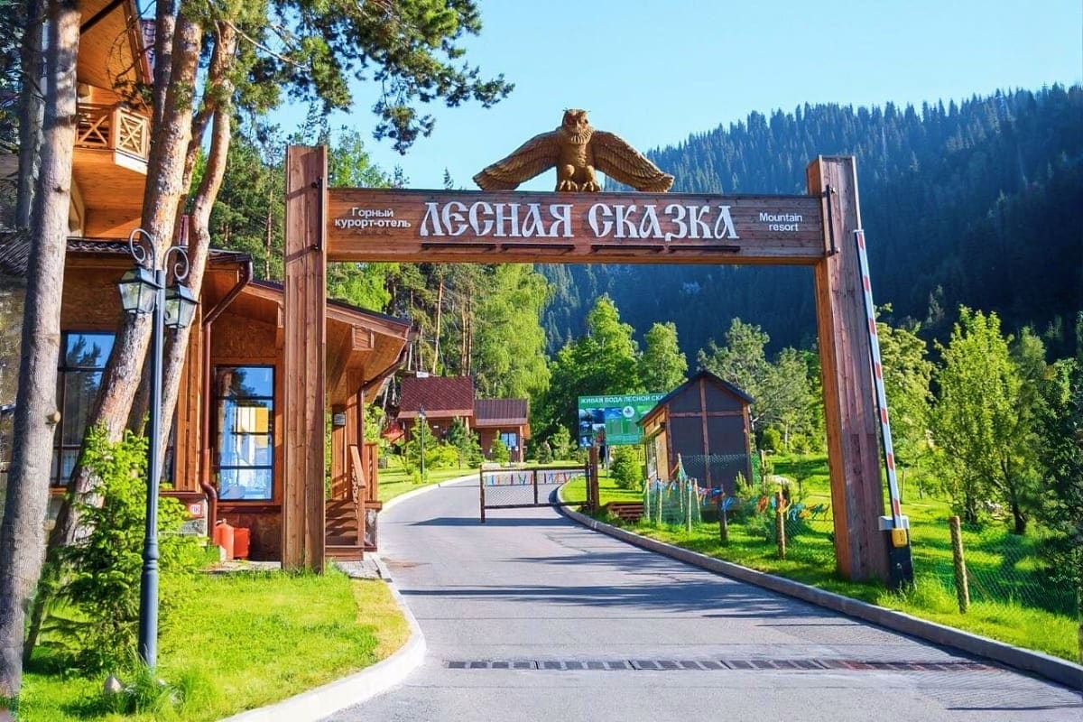Wooden entrance gate with eagle sculpture at Lesnaya Skazka mountain resort surrounded by pine forest and green meadow