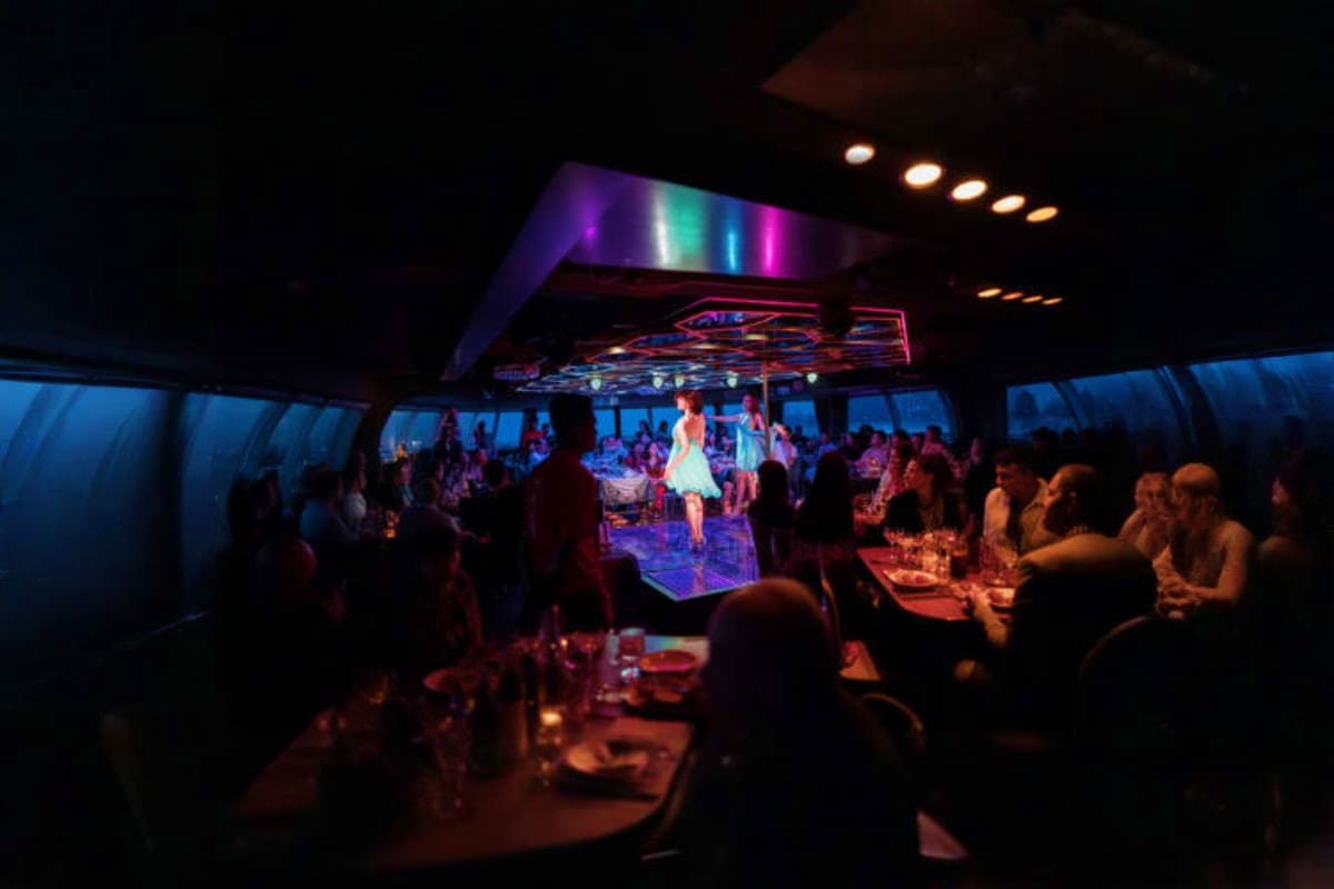 All star cruise Guests dancing and dining in an illuminated nightclub venue aboard All Star Cruise ship with colorful stage lighting and ocea