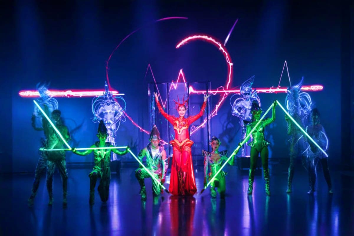 Neon-lit cabaret performers on stage with glowing geometric set design and dramatic lighting at Calypso Bangkok theater show