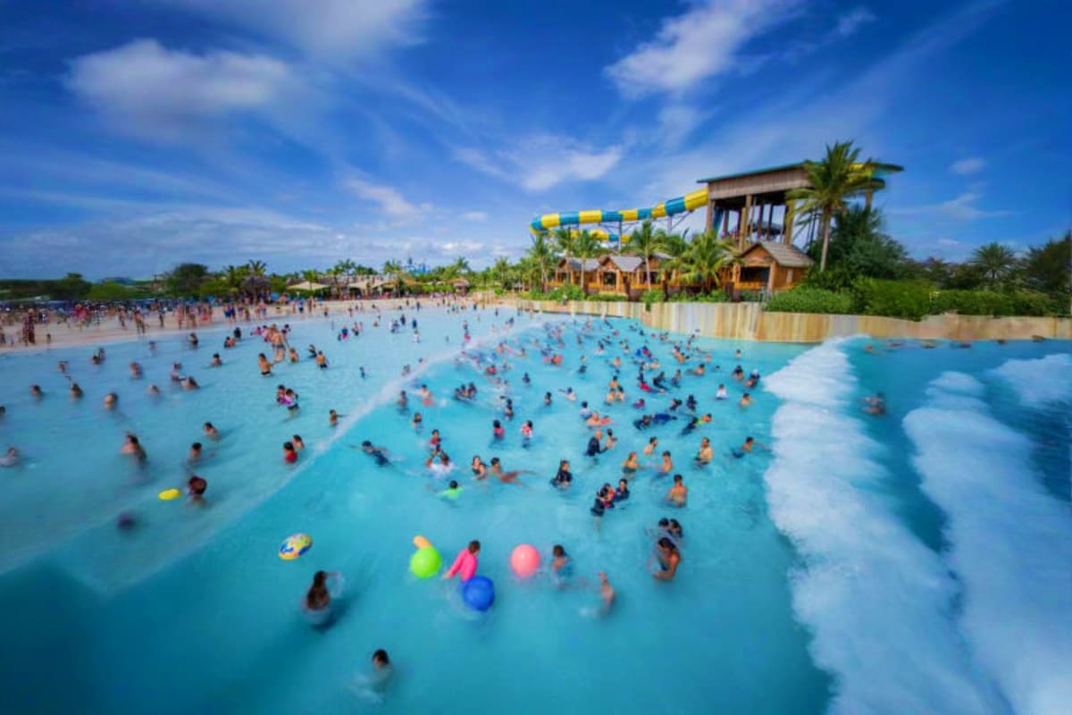 Andamanda Phuket Crowded water park with turquoise pools, white foam waves, swimmers and floaties, wooden structure with blue and yellow slide