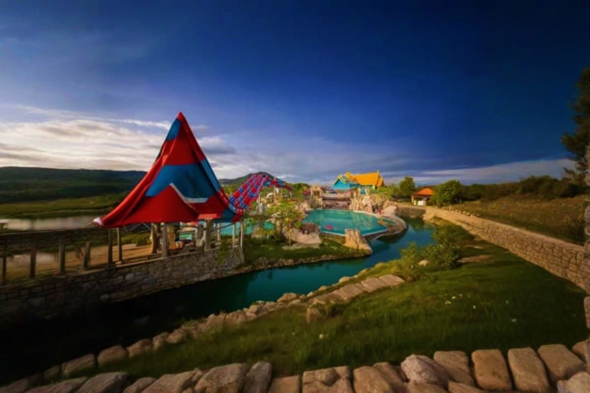 Andamanda Phuket Colorful water park with red and blue tent-like structure, turquoise pools, yellow roof building, and green landscaping besid