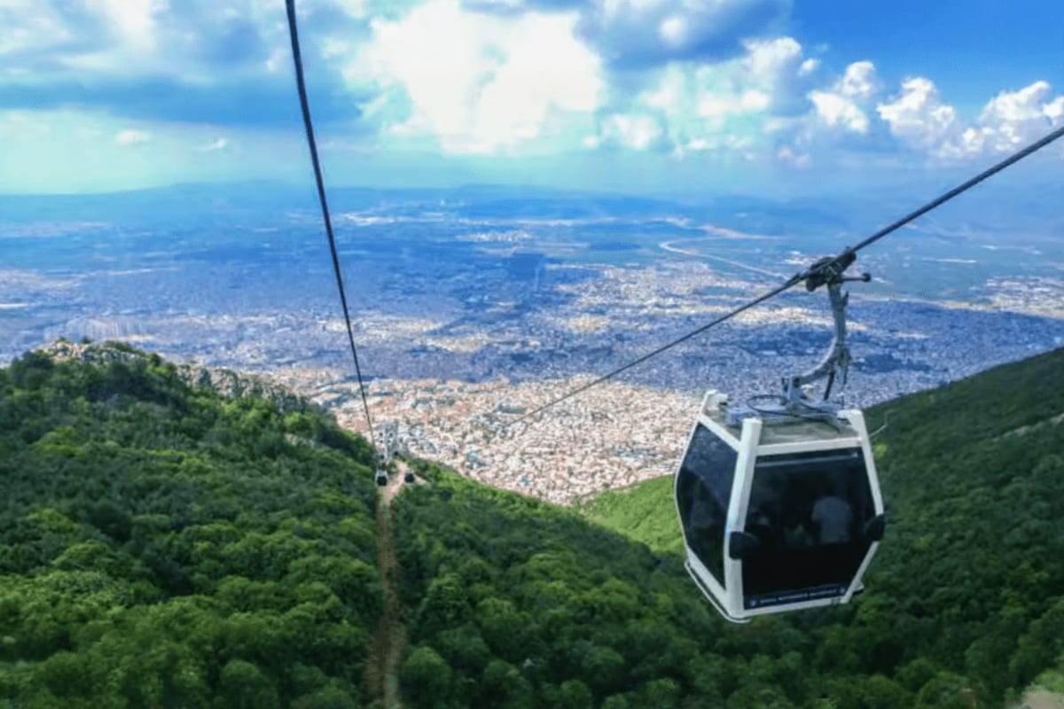 Cable car ascending Uludag mountain with panoramic view of Bursa city sprawling across the valley below under blue sky