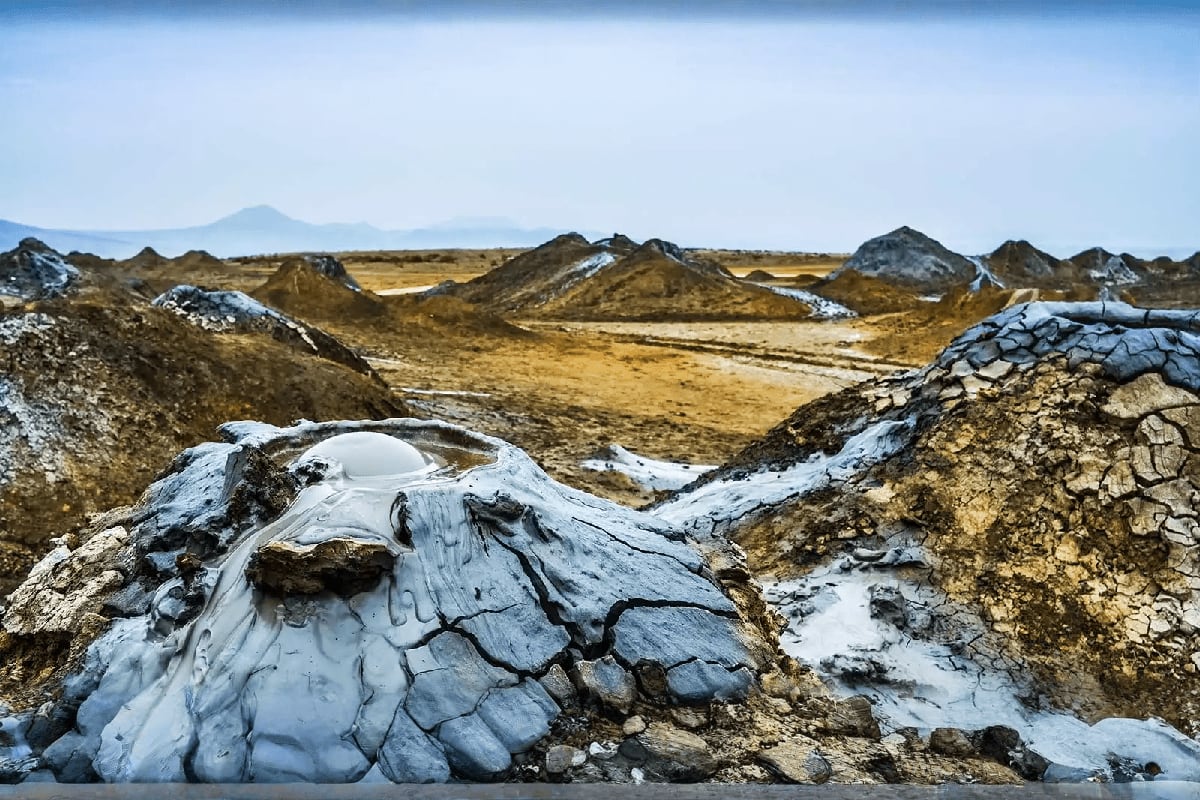 Gobustan mud volcano landscape with white and gray bubbling mud formations, brown hills, patches of snow, and distant mountai