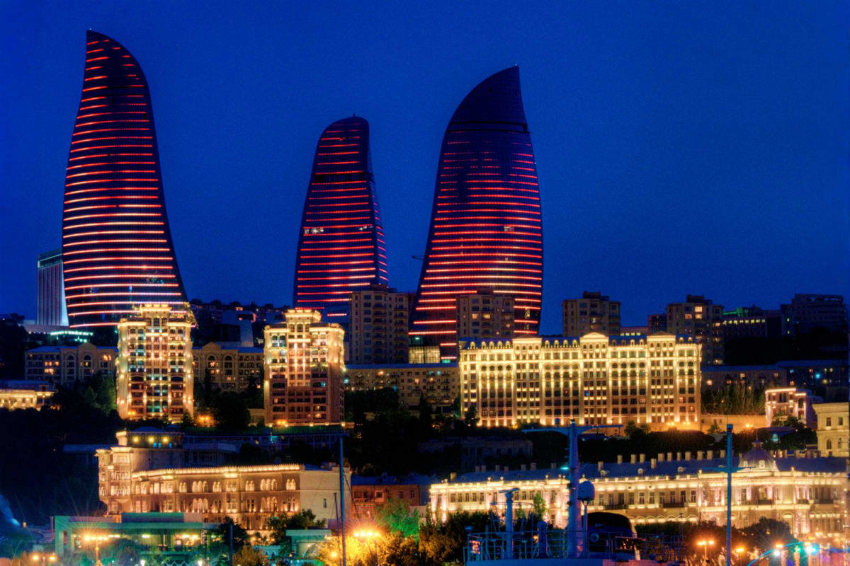 Baku skyline at night with illuminated Flame Towers and historic Old City buildings lit up against dark blue sky