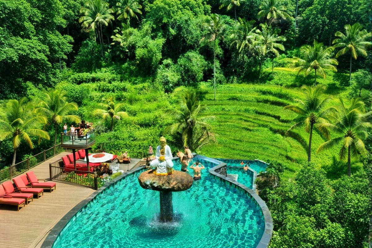 Aerial view of D Tukad Coffee Club resort in Ubud showing turquoise pool with central fountain, red loungers on wooden deck,