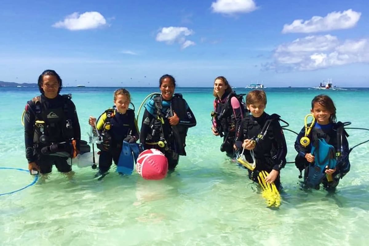Family and instructor in scuba diving gear wading into turquoise tropical waters for a guided diving lesson