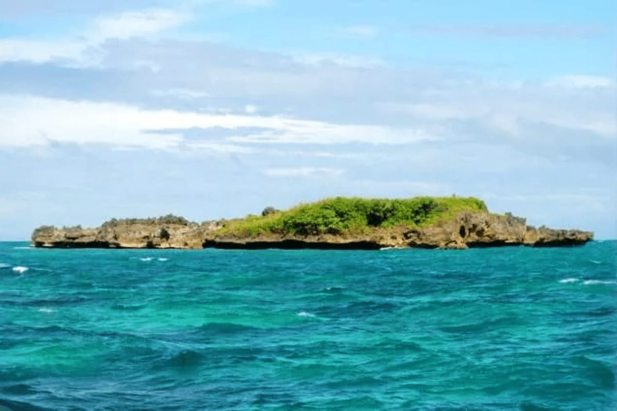 Rocky island with green vegetation surrounded by turquoise waters under blue sky with white clouds