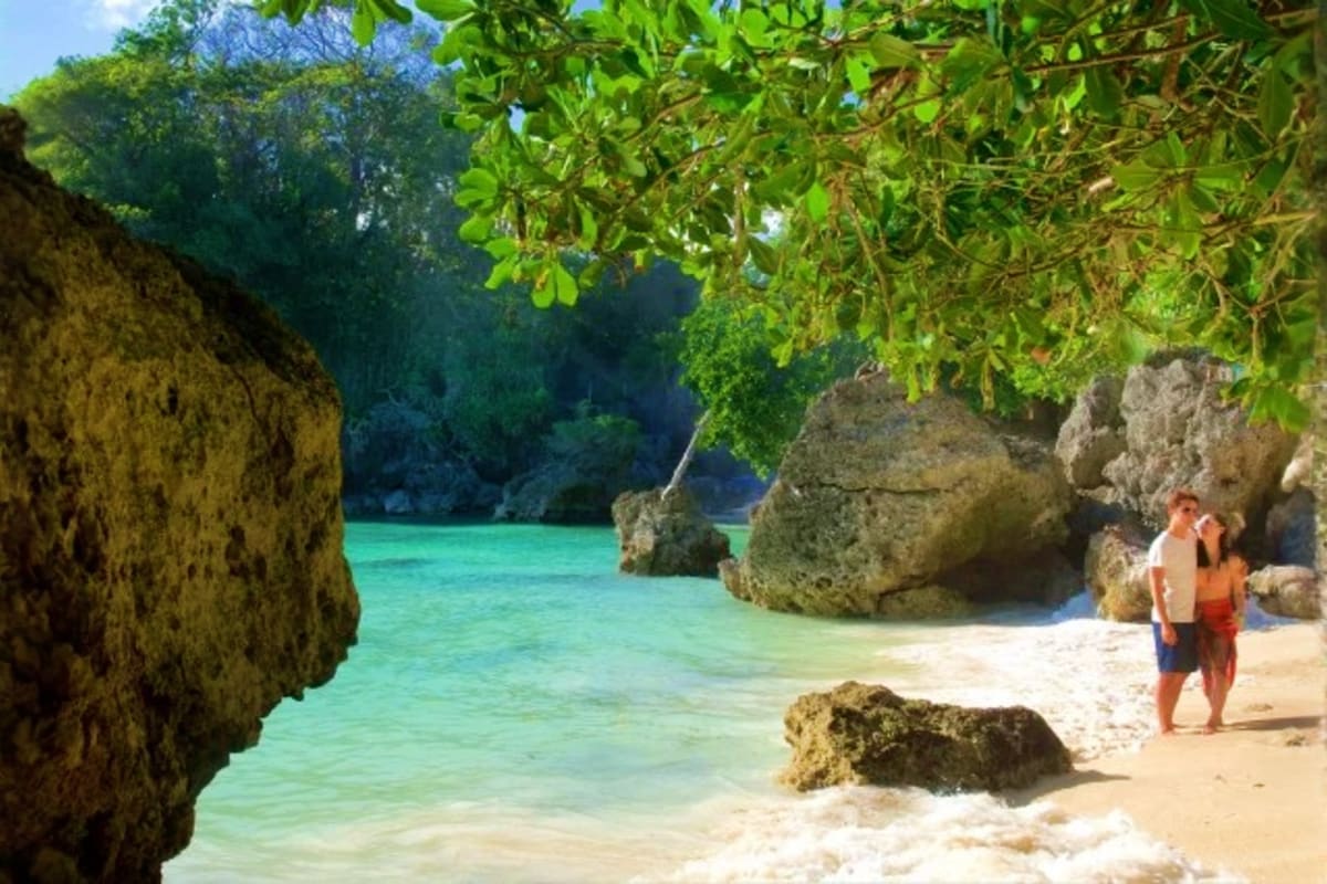 Couple standing on white sand beach surrounded by limestone rock formations and turquoise water at tropical island cove