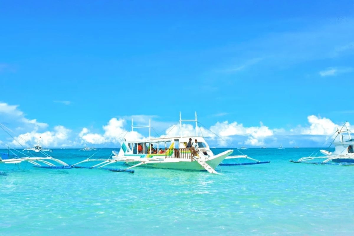 Traditional Filipino outrigger boat with tourists anchored in turquoise shallow water during island hopping tour in Boracay
