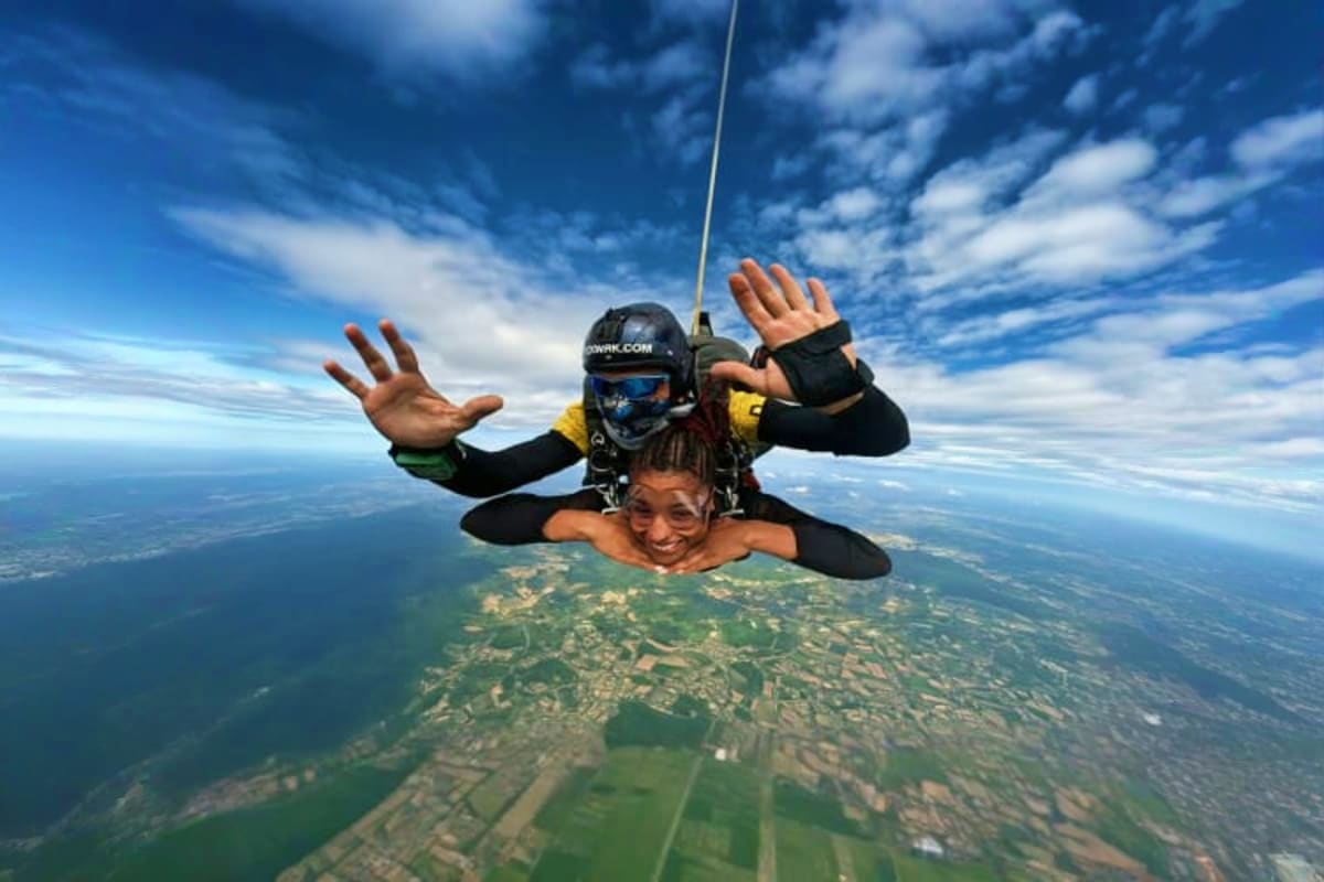 Tandem skydiving instructor and student freefalling above patchwork farmland with blue sky and clouds
