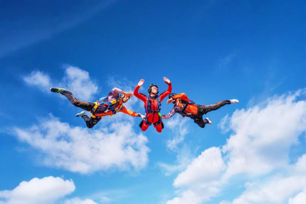 Three skydivers in colorful jumpsuits freefalling through clear blue sky with white clouds during a skydiving adventure