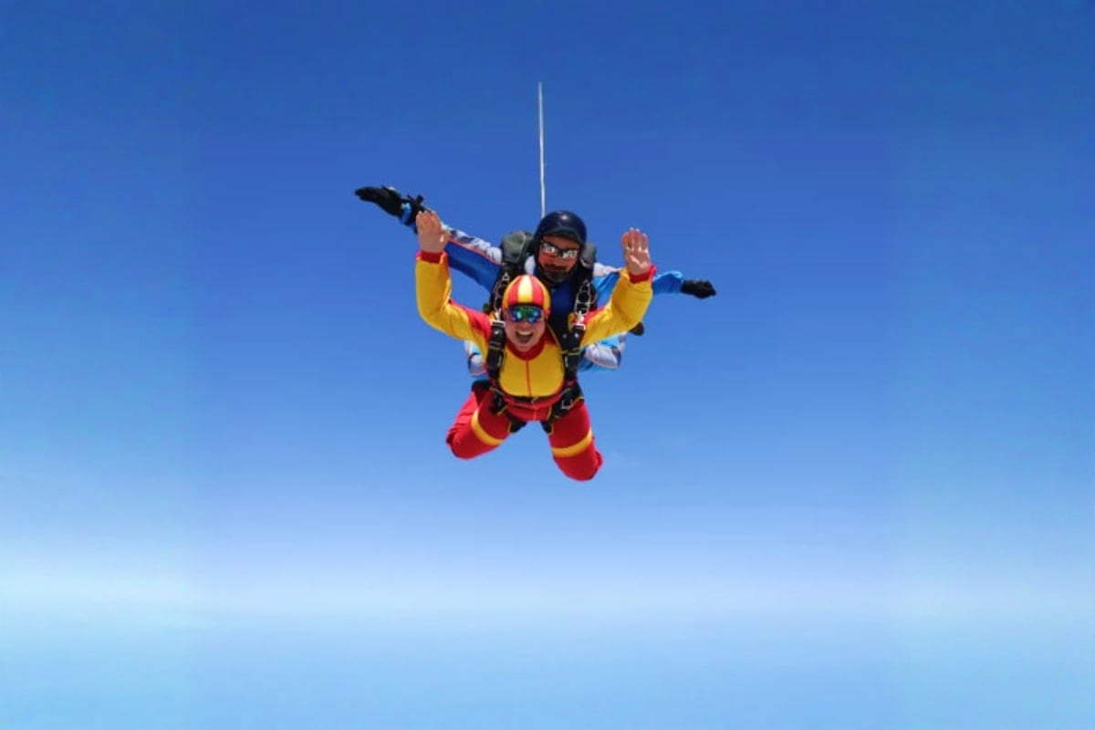 Tandem skydiving jump with instructor and student in yellow and red gear against clear blue sky