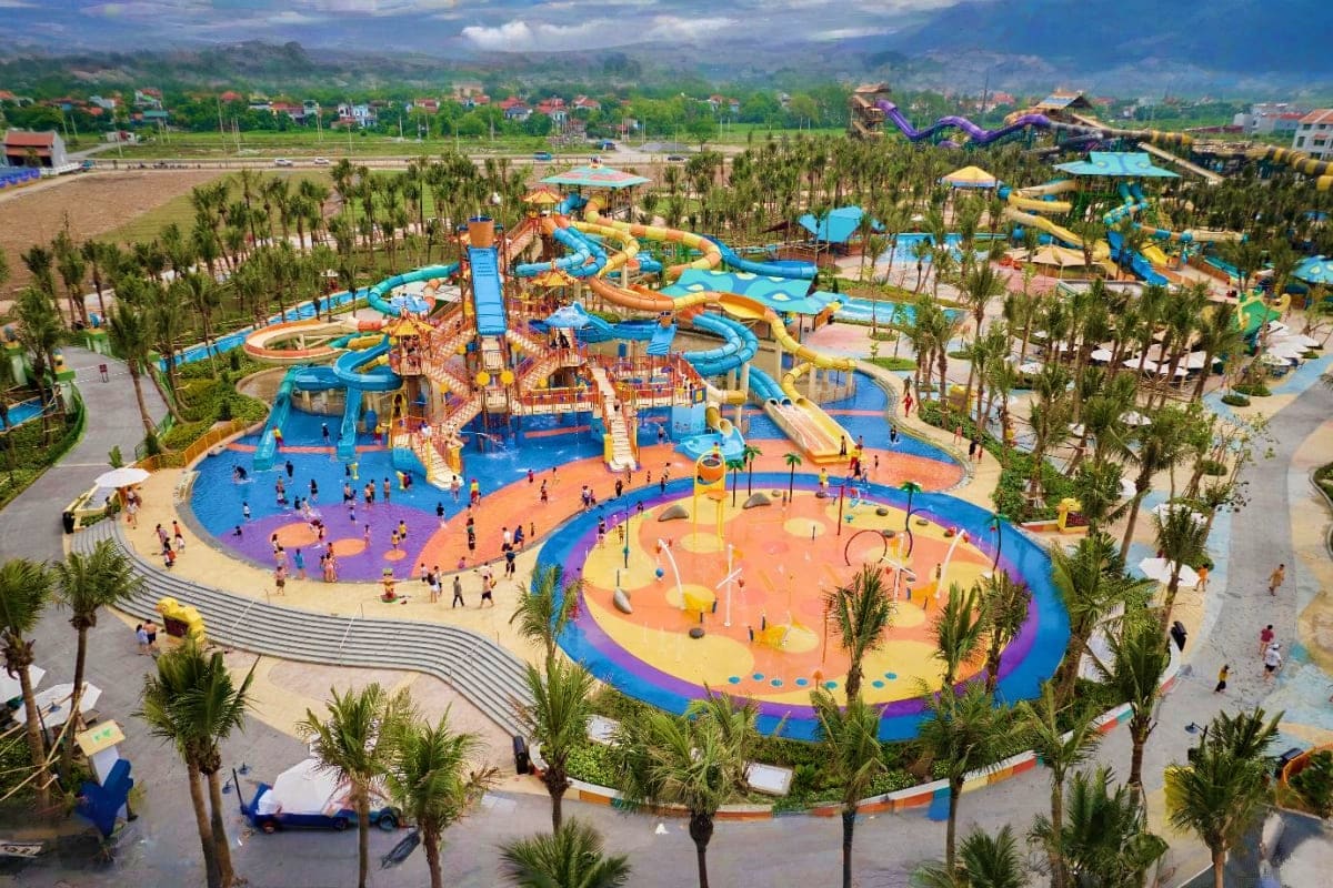 Sun World Ha Nam Aerial view of Sun World Ha Nam water park with colorful slides, pools, and palm trees surrounded by mountains and residentia