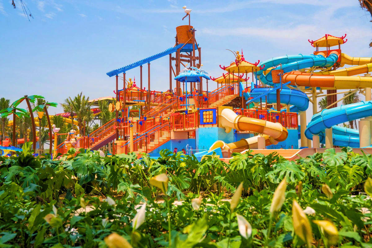 Sun World Ha Nam Colorful water park with orange and blue slides, pagoda-style towers, and palm trees under clear sky at Sun World Ha Nam