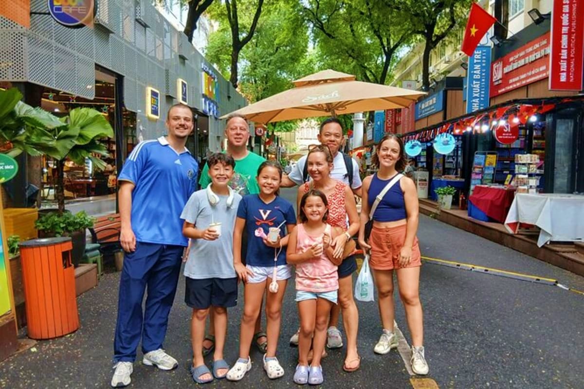 Ho Chi Minh Full day Sharing Tour Group of tourists posing on a pedestrian street in Ho Chi Minh City with shops and Vietnamese flags visible