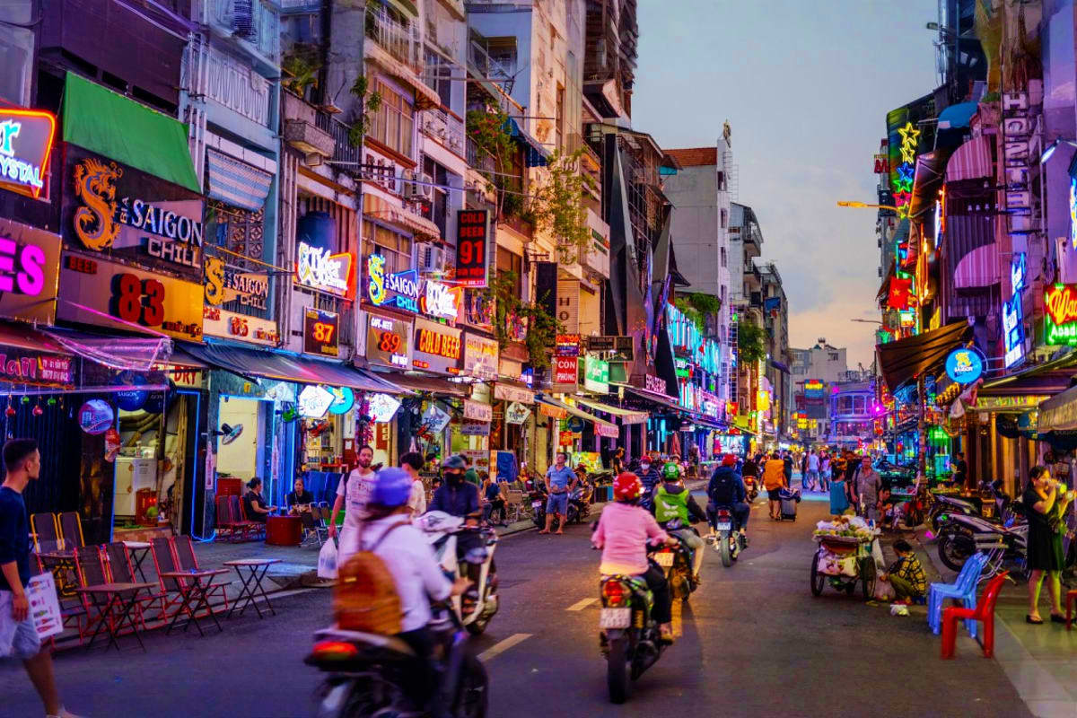 Ho Chi Minh Full day Sharing Tour Bustling Ho Chi Minh City street with colorful neon signs, motorbikes, and pedestrians in a busy shopping and entertainment d