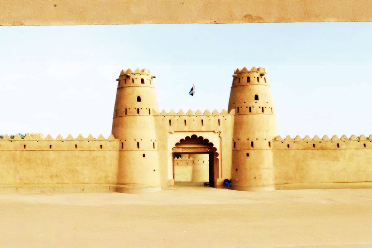 Ancient mud-brick fort with two round towers and crenellated walls in desert landscape, UAE heritage architecture