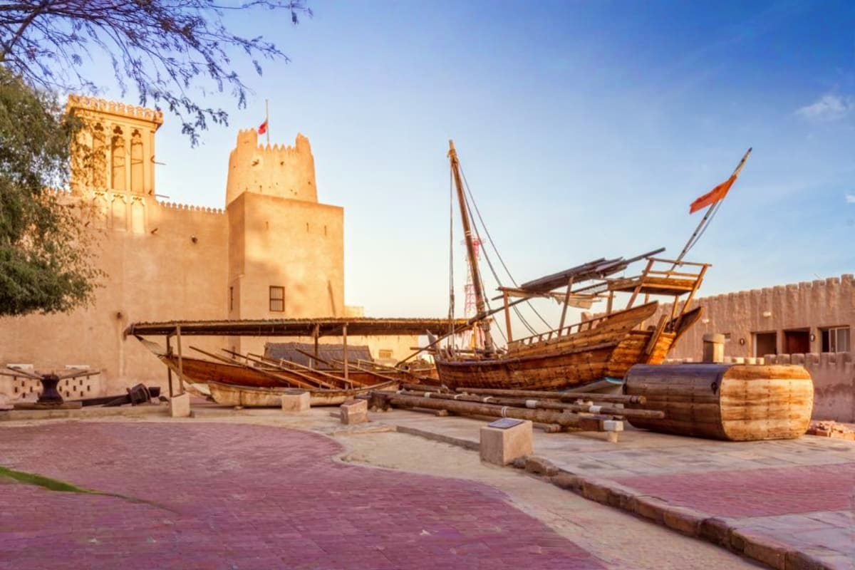 Historic wooden dhow boats displayed in courtyard with traditional Arabian fort and crenellated walls in background