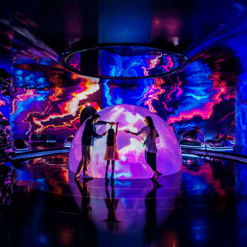 Silhouettes of visitors inside a glowing purple dome surrounded by vibrant blue and pink digital art projections at AYA Unive