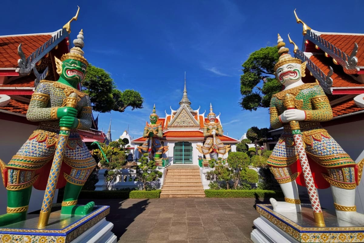 Bangkok City Tour Thai temple courtyard with ornate demon guardian statues and traditional architecture with golden spires and orange tile roof