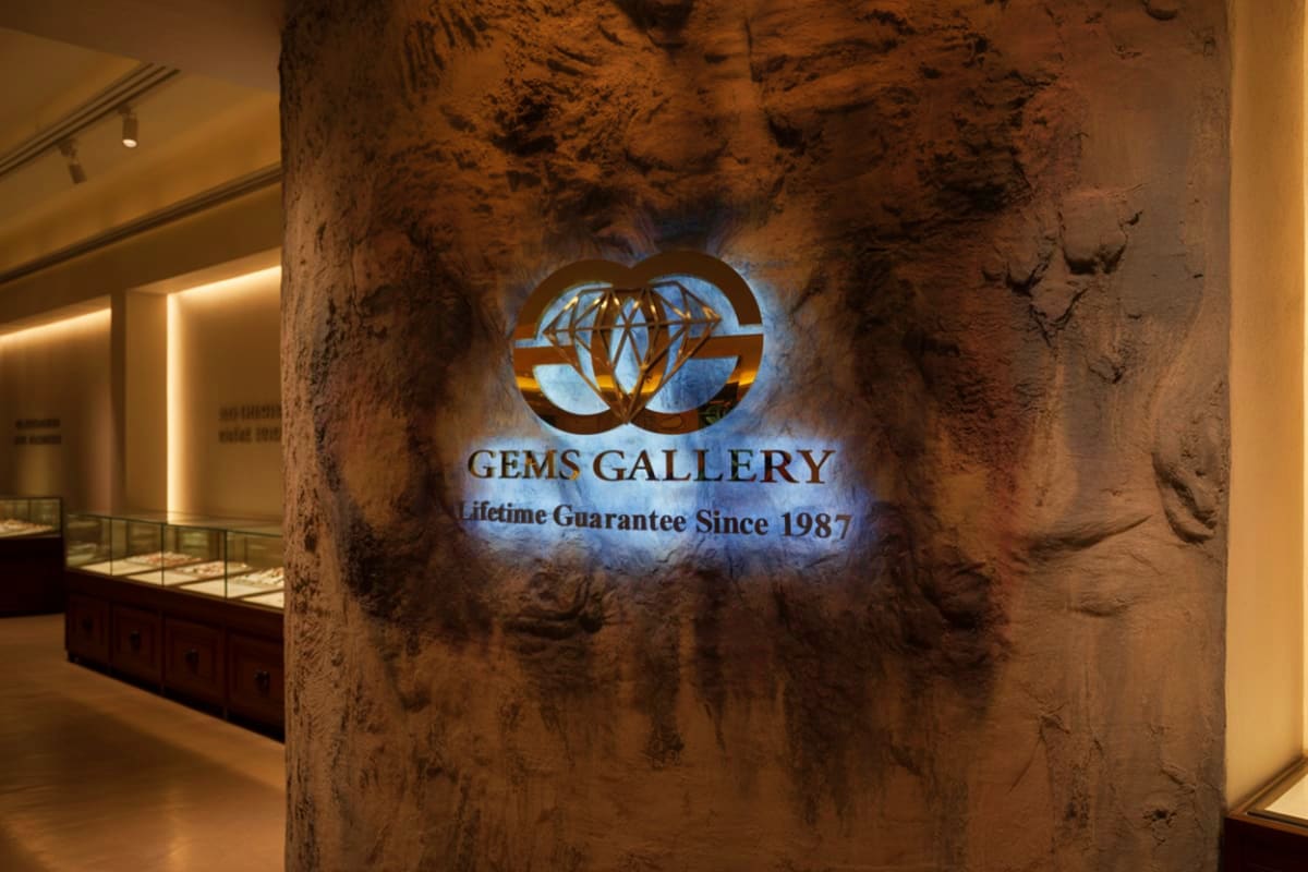 Bangkok City Tour Gems Gallery storefront sign with illuminated logo on textured brown wall, displaying "Lifetime Guarantee Since 1987" in upsc