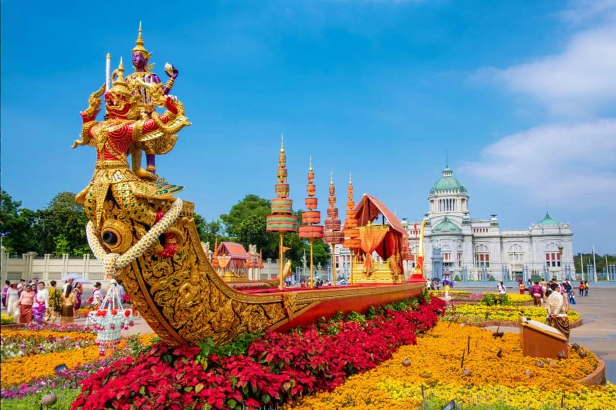 Bangkok City Tour Golden ornate barge sculpture with Thai mythical figures surrounded by colorful flower gardens, Bangkok royal palace in backg