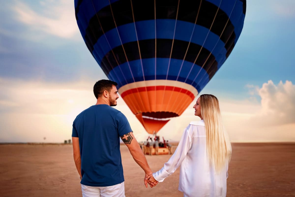 Breakfast in the sky with Balloon flights Couple holding hands watching a blue and orange hot air balloon preparing for flight on a desert landscape at dawn