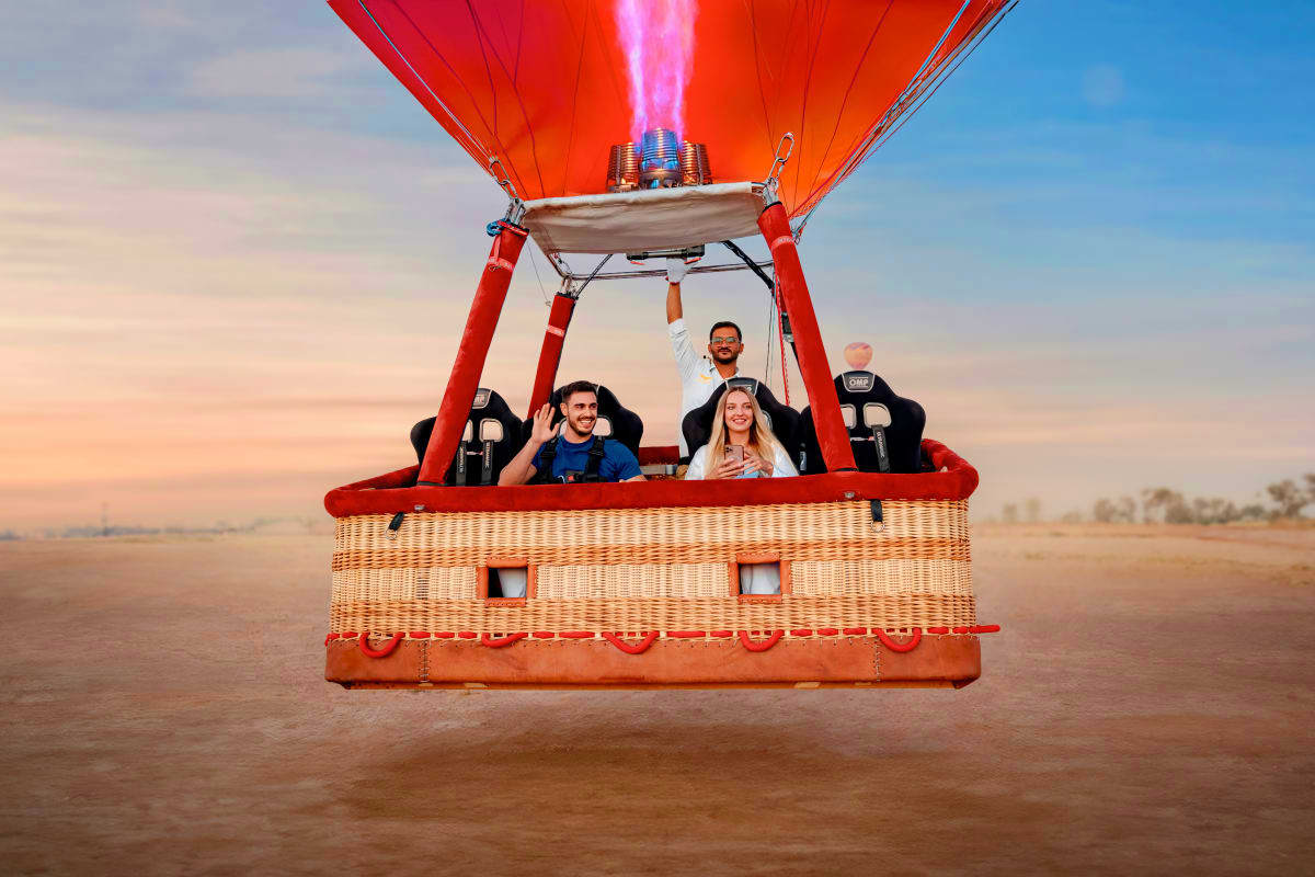 Breakfast in the sky with Balloon flights Four people in a red and wicker hot air balloon basket with burner flame active, floating above desert landscape at sunrise