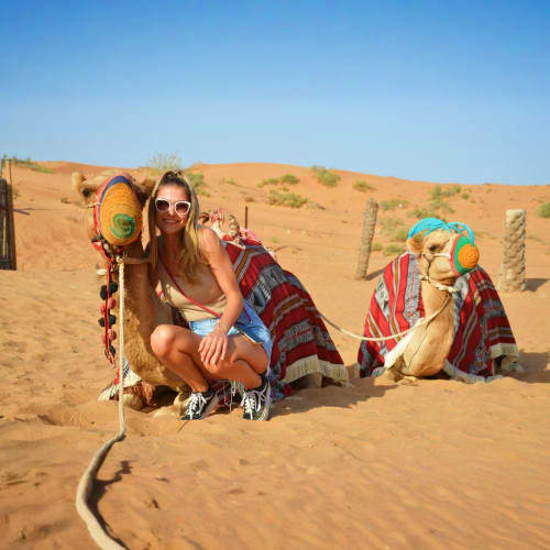 Woman posing with decorated camels in desert sand dunes during camel ride tour in Ras Al Khaimah