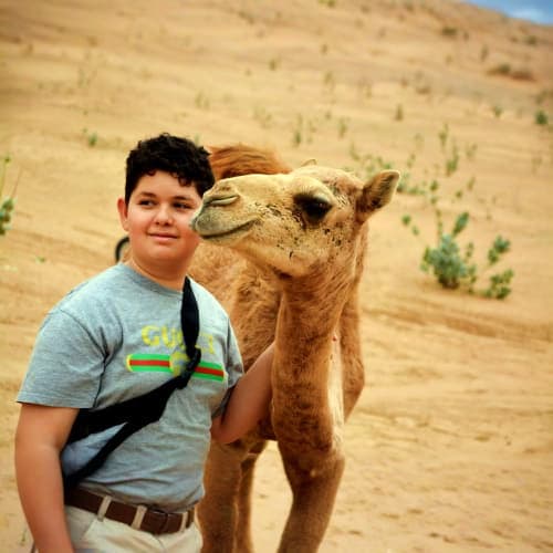 Young boy posing with a camel in a desert landscape during a camel ride tour in Ras Al Khaimah
