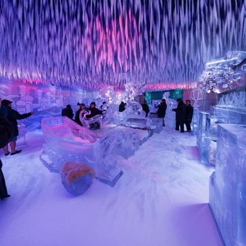 Chillout Ice Lounge Dubai Visitors inside an ice lounge with illuminated purple and pink lighting, ice sculptures, and frozen furniture in a winter-the