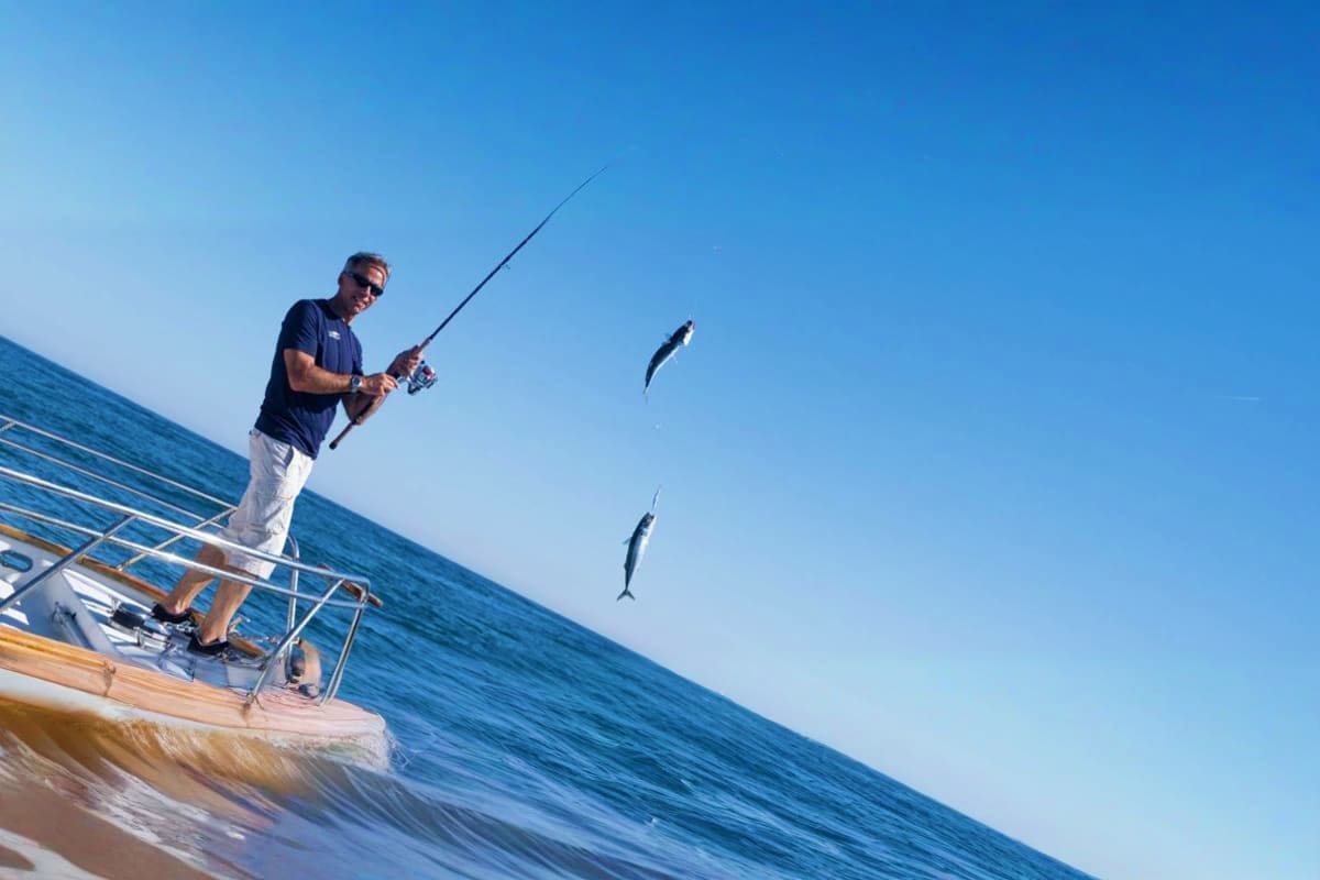 Man fishing from boat with two fish jumping out of water in clear blue ocean