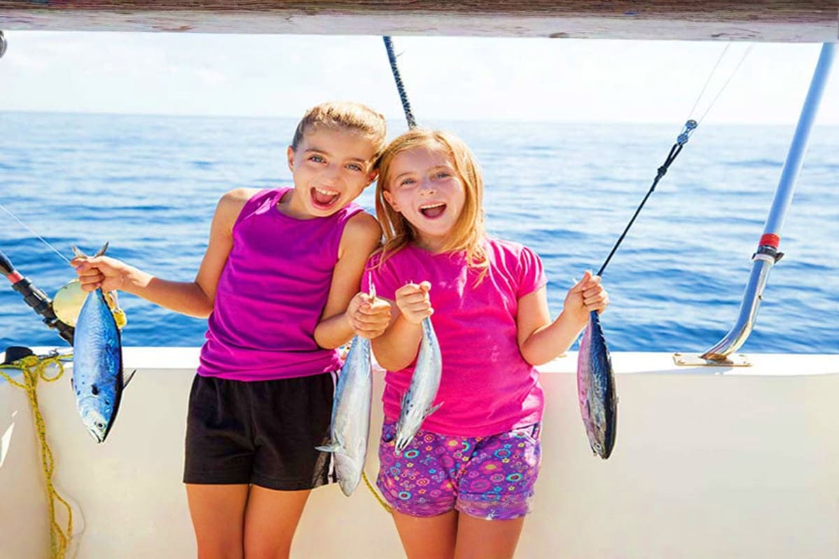 Two young girls holding caught fish on a deep sea fishing boat with ocean water in the background