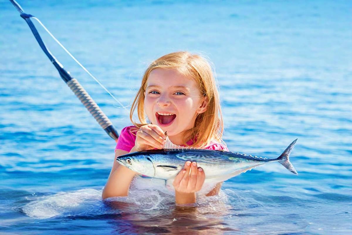 Young girl in ocean holding a mackerel fish with fishing rod while standing in shallow water