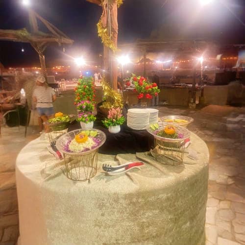 Evening outdoor dinner setup with floral centerpiece, place settings, and string lights at desert safari venue in Ras Al Khai