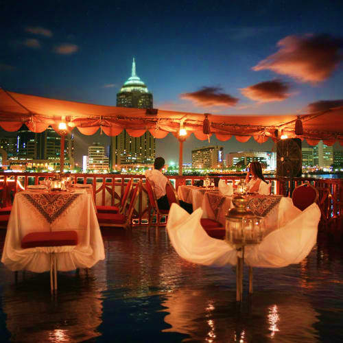 Rooftop dinner setup with city skyline and illuminated building at dusk, elegant table settings with white linens overlooking