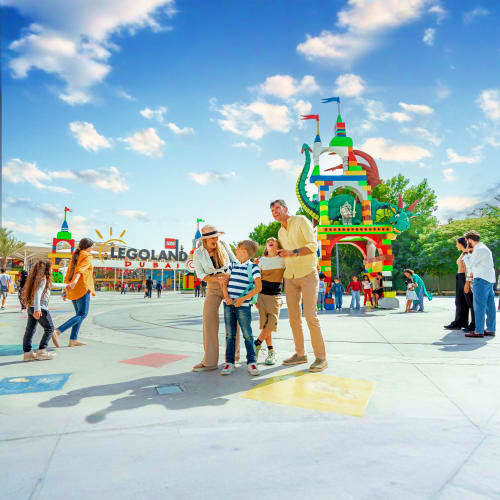 Family enjoying LEGOLAND Dubai entrance area with colorful brick castle structure and themed attractions on sunny day