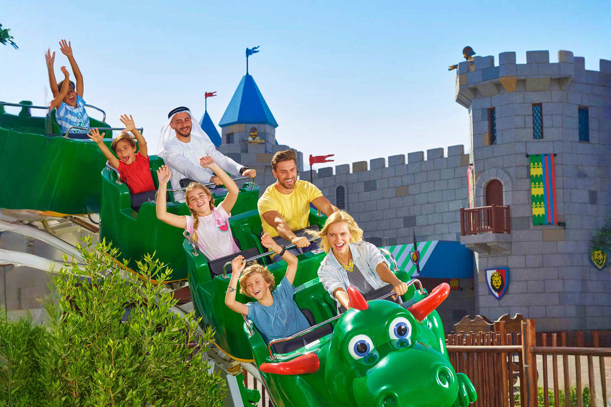Family enjoying green dragon roller coaster ride at Dubai Parks and Resorts with castle fortress in background
