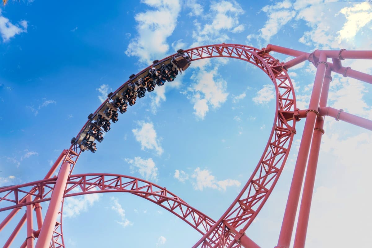 Roller coaster riders experience a steep climb on a red steel track against a blue sky at Dubai Parks and Resorts.