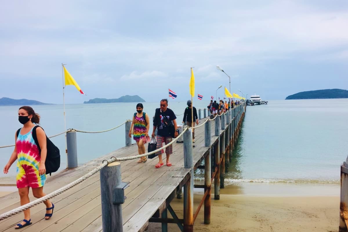 Ferry Tickets for Koh Samui Pier to Koh Tao Maehaad Tourists walking on wooden pier at Koh Samui with yellow and Thai flags, boats and islands visible across calm turquoise wate