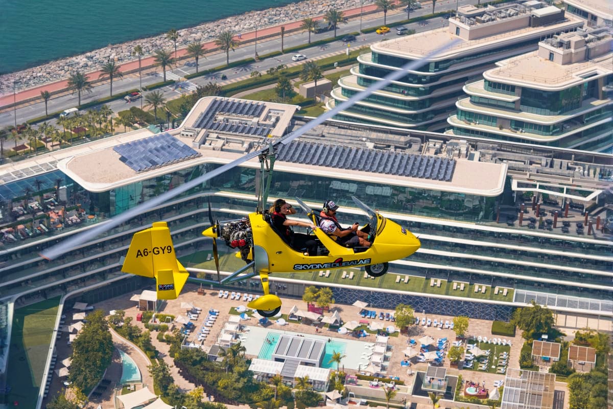 Gyrocopter Flight In Dubai Yellow gyrocopter flying over Dubai beachfront with modern high-rise buildings, palm trees, and beach below