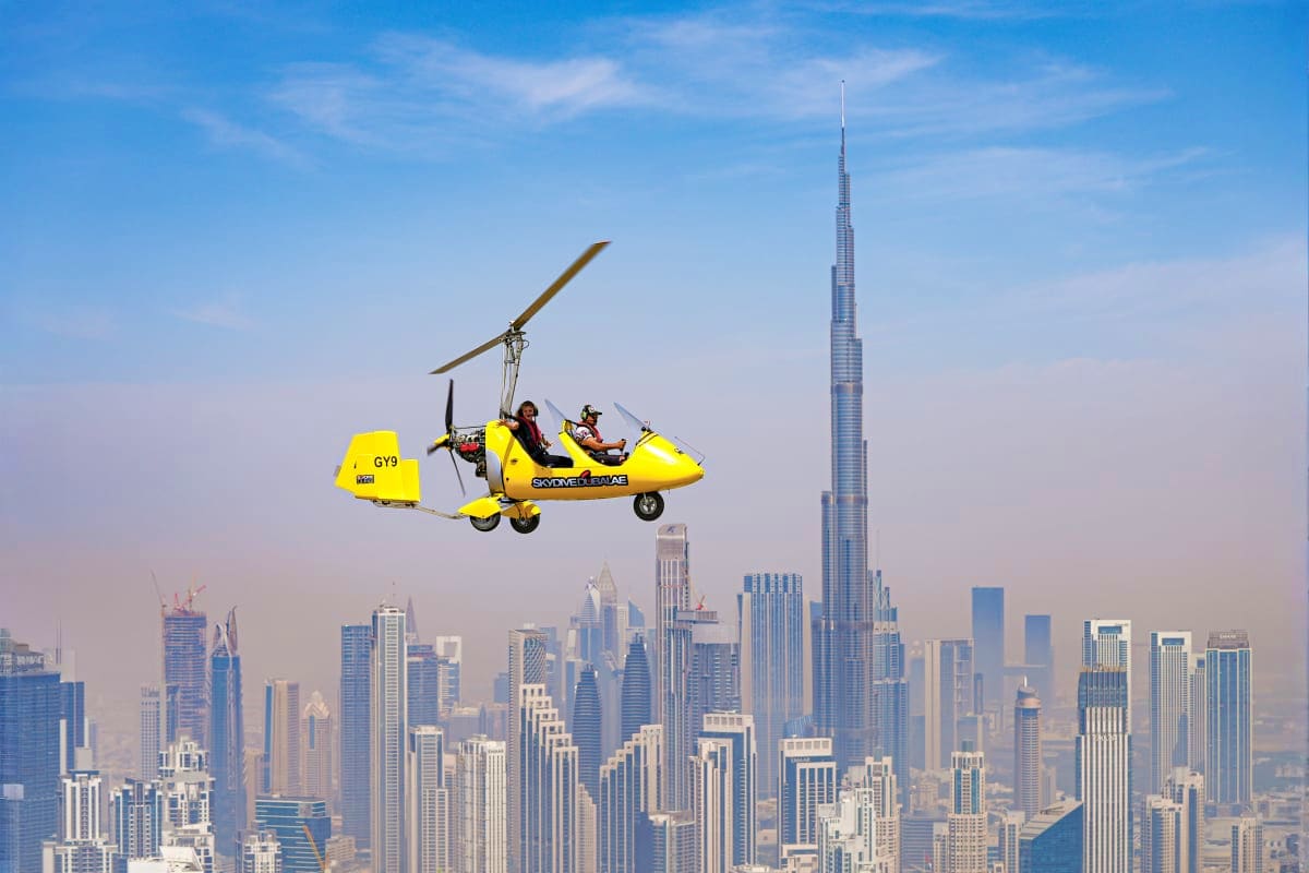 Gyrocopter Flight In Dubai Yellow gyrocopter flying over Dubai cityscape with Burj Khalifa and modern skyscrapers visible below against blue sky
