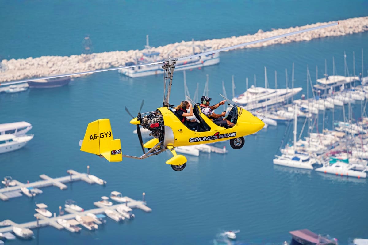 Gyrocopter Flight In Dubai Yellow gyrocopter flying over Dubai marina with moored boats and white breakwater below