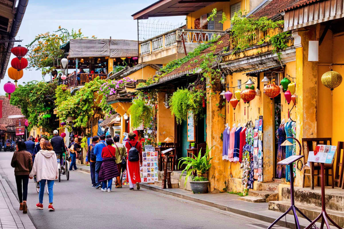Hoi An and Cam Nam Trip Tourists walking through Hoi An Ancient Town with yellow French colonial buildings, colorful lanterns, ivy-covered facades, a