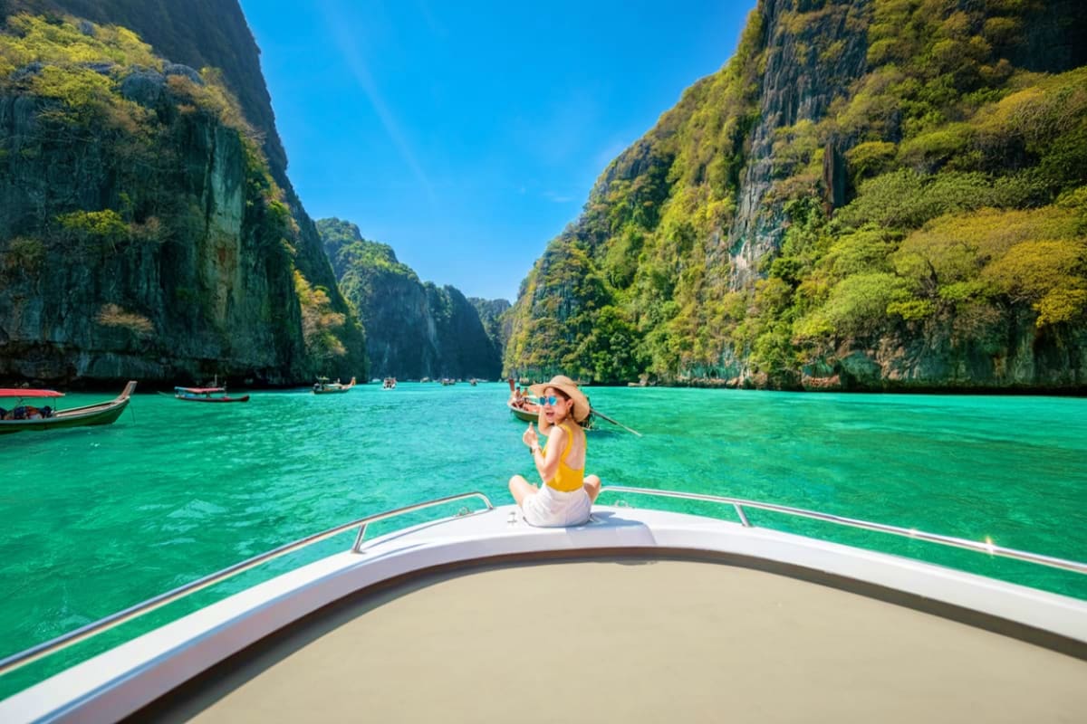 Woman on speedboat in emerald waters surrounded by limestone cliffs at Hong Island, Thailand